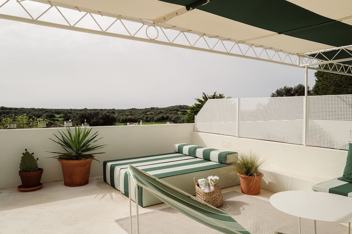 A rooftop terrace with a green-striped sofa, potted plants, and a white table.