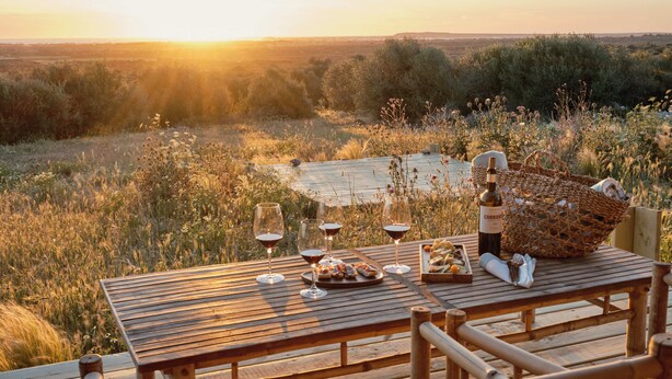 A wooden table set for a meal with wine glasses, a basket, and a bottle of wine. - Hotel Rural Morvedra Nou (Ciutadella de Menorca)