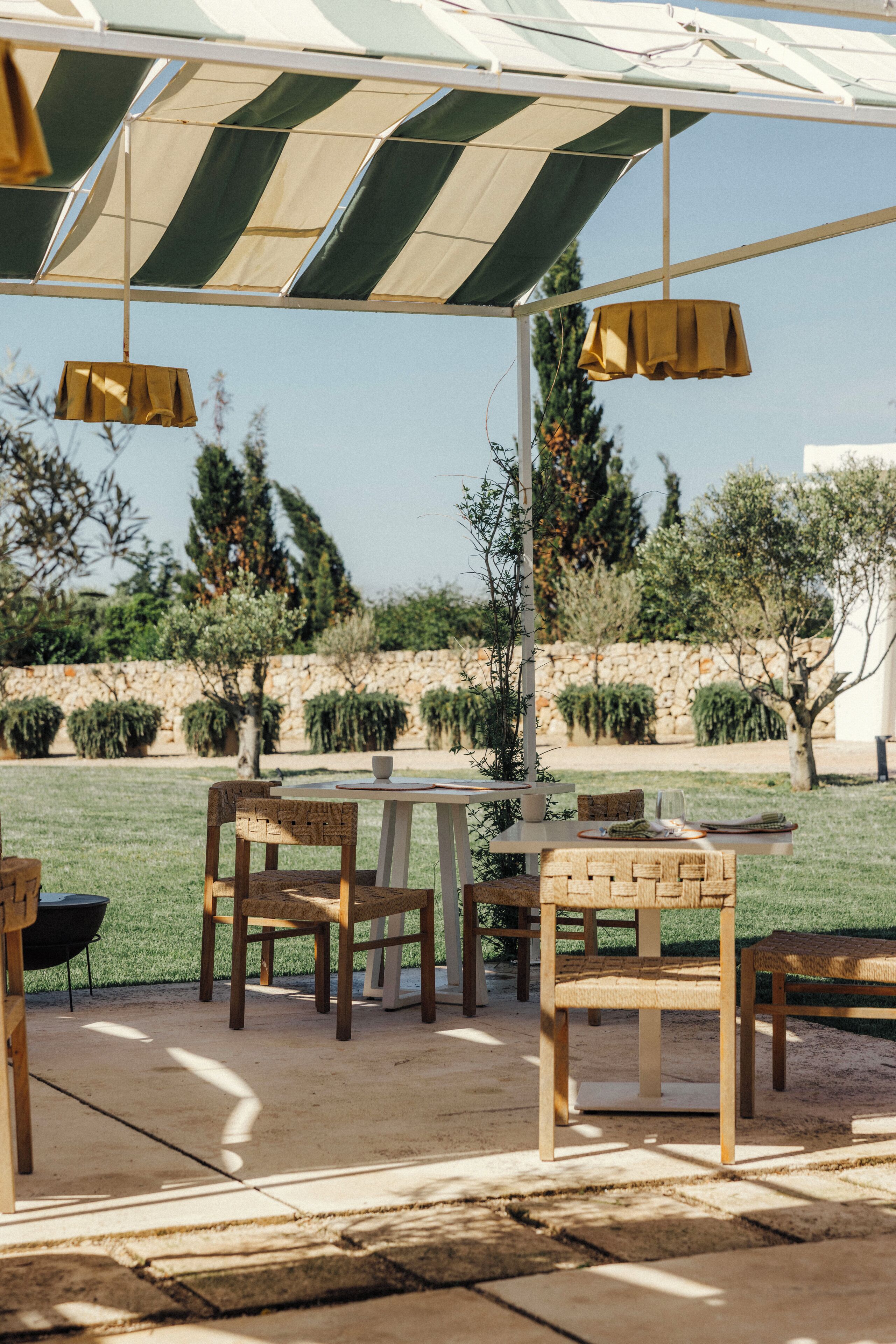 An outdoor patio area with tables and chairs, a covered seating area, and a view of a landscaped garden.