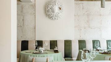 Un comedor con mesas y sillas a rayas verdes, una pared blanca con un adorno decorativo y una pared de ladrillo rústico.