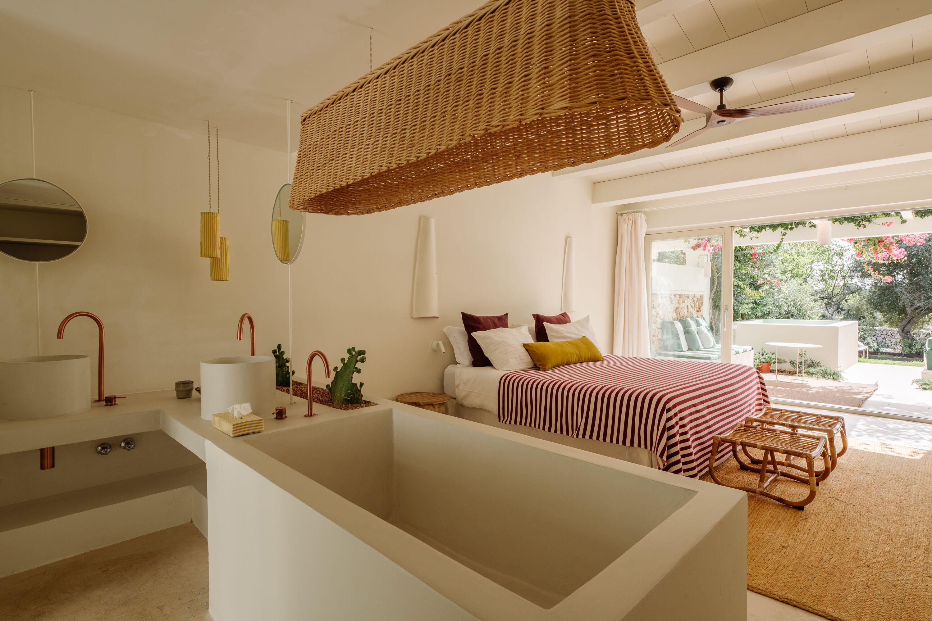 Un dormitorio moderno con una bañera grande, una cama con ropa de cama a rayas y un ventilador de techo de mimbre.