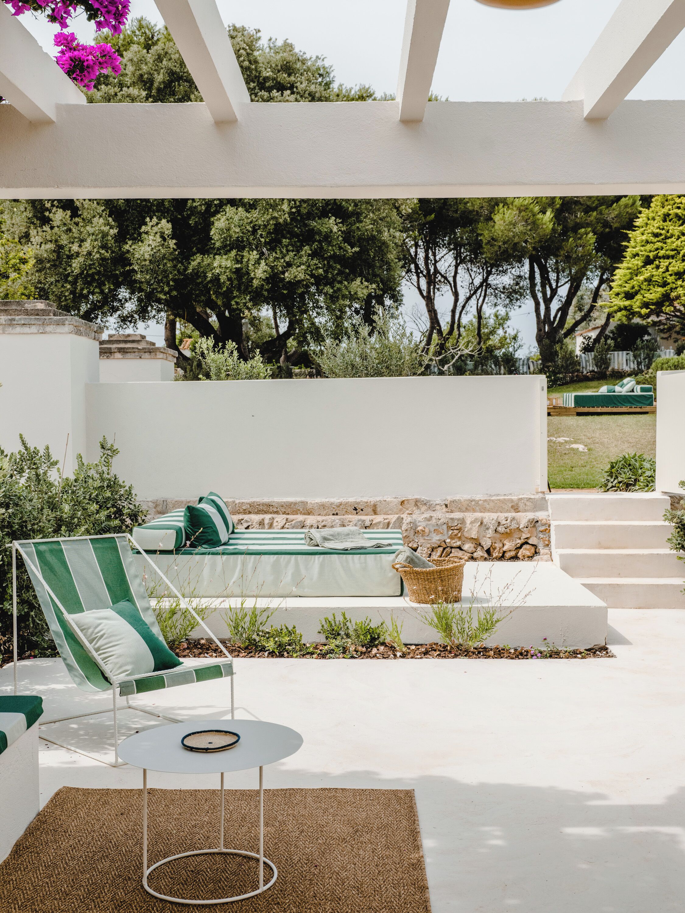 A patio with a lounge chair, a small round table, and a bed with a green-striped cushion.