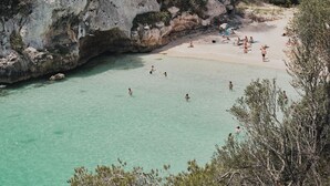 A beach with clear turquoise water, rocky cliffs, and sparse vegetation. - Hotel Rural Morvedra Nou (Ciutadella de Menorca)