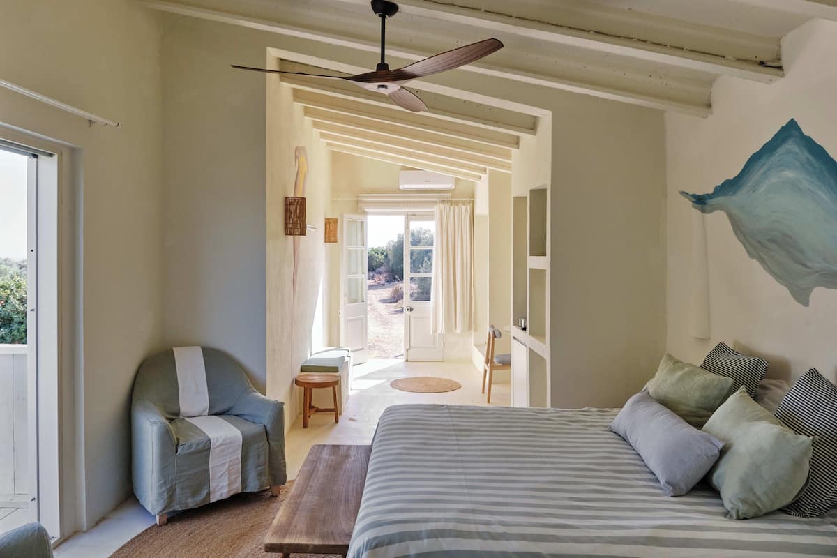 A bedroom with a bed, a chair, a ceiling fan, and a view of the outdoors.