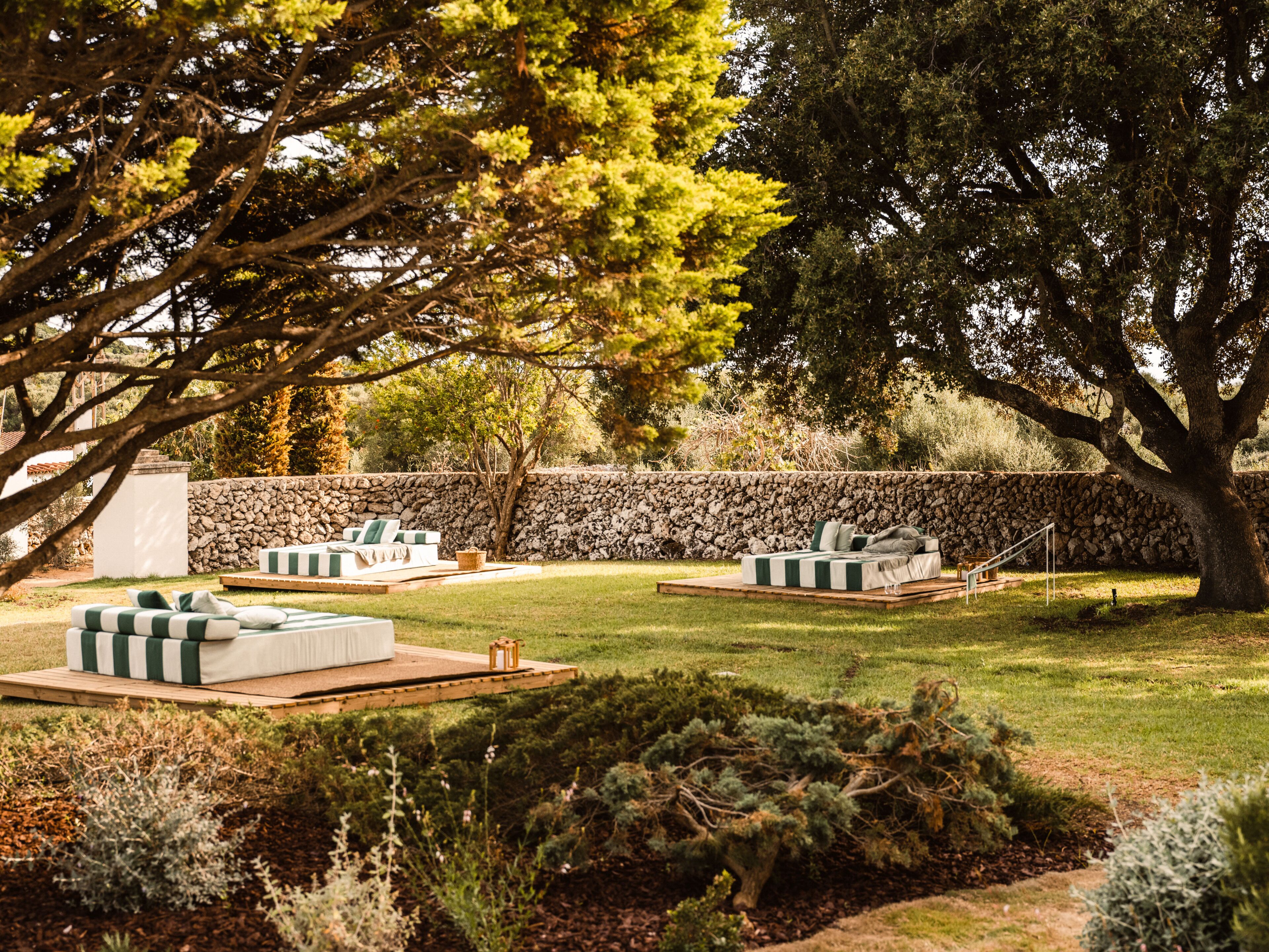 Un jardín con dos zonas de estar al aire libre, un muro de piedra y un gran árbol.