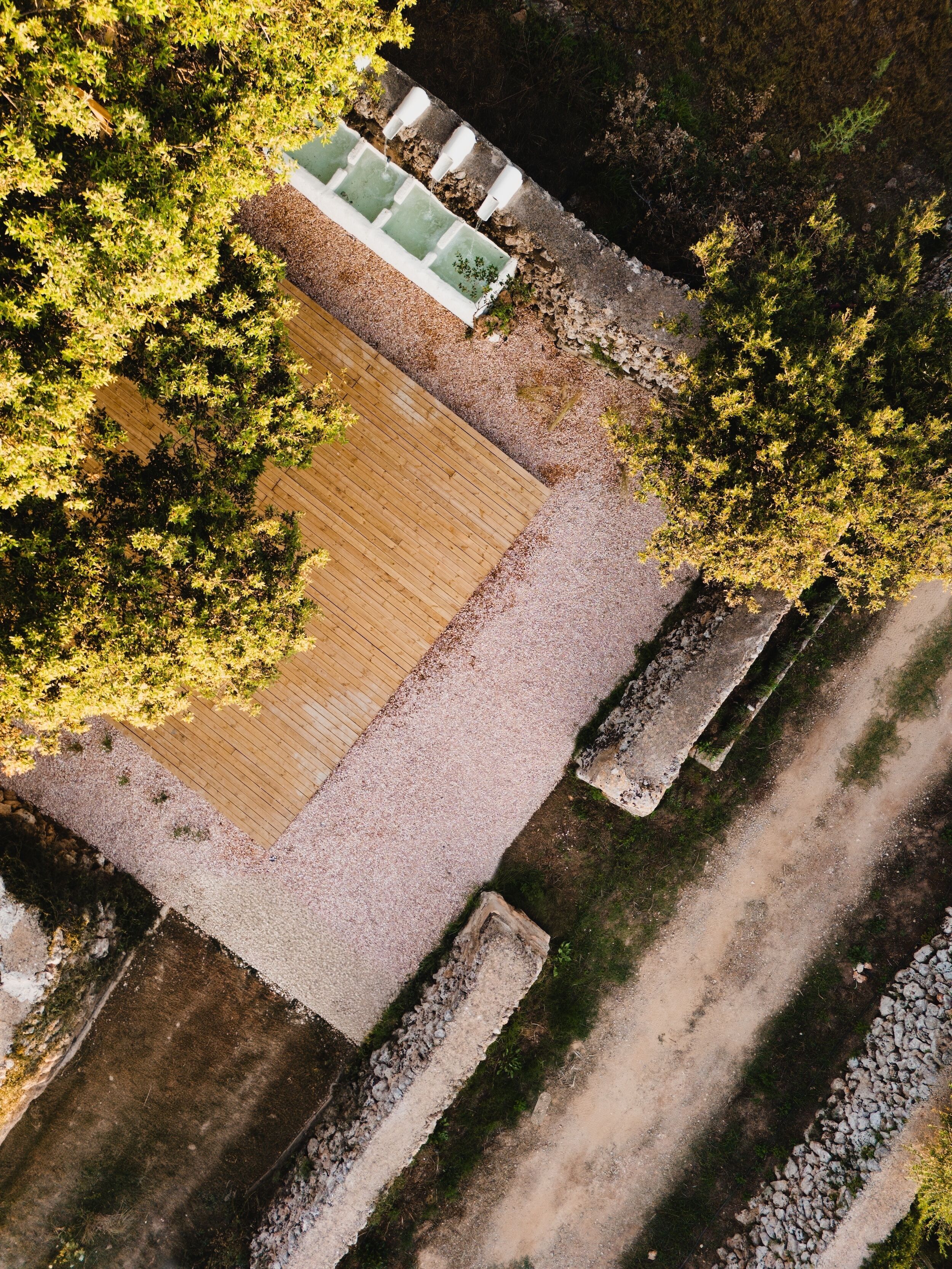Vista aerea di un cortile con un molo in legno, un percorso in pietra e vegetazione circostante.