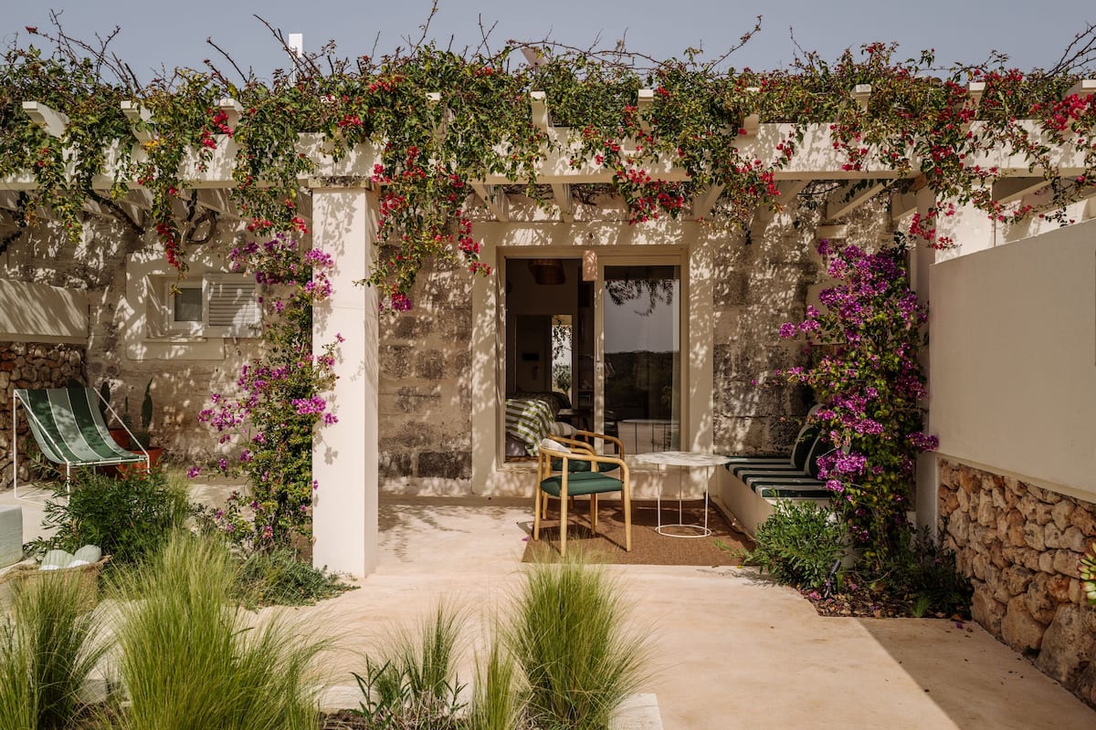 A covered outdoor seating area with a chair and table, surrounded by lush greenery and flowering plants.
