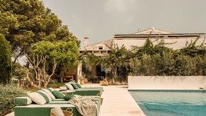 A poolside area with a green sofa set, a wicker basket, and a clear blue pool. - Hotel Rural Morvedra Nou (Ciutadella de Menorca)