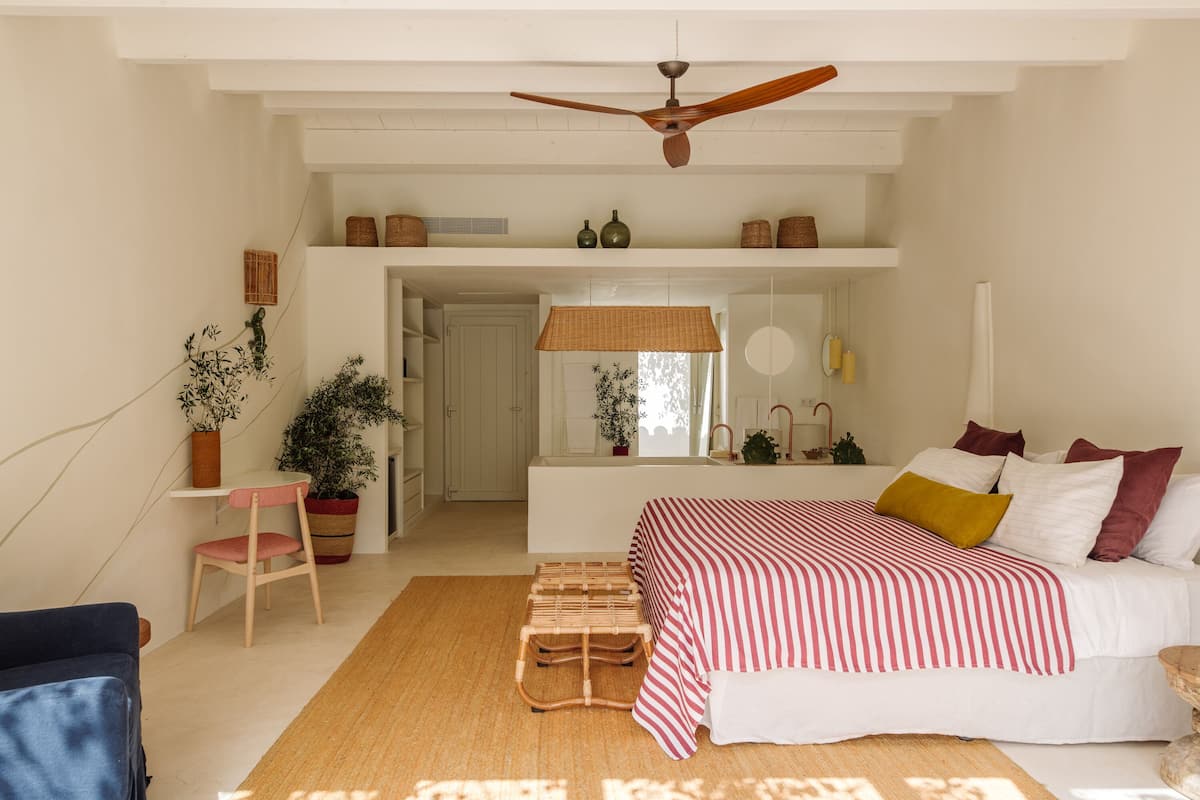 A spacious bedroom with a large bed, a ceiling fan, and a view into the bathroom.