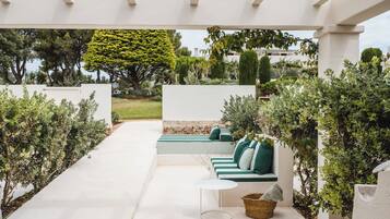 Un espacio de estar al aire libre cubierto con una pérgola blanca, un banco de piedra y una cesta de mimbre.
