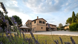 A large two-story building with a flat roof and a central chimney, surrounded by a well-maintained lawn and lavender bushes. - Agriturismo Ai Prati (Perugia)