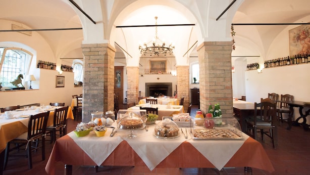 A dining area with tables set for a meal, a chandelier, and a fireplace in the background. - Agriturismo Ai Prati (Perugia)