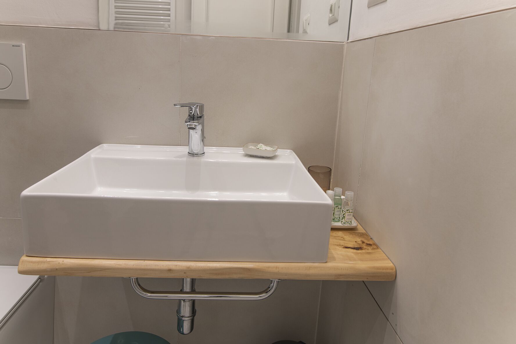 Ein Badezimmer mit einem weißen Waschbecken, einem Holzregal und einer Metallrohrleitung.