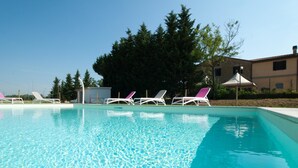 A swimming pool with clear blue water, surrounded by white lounge chairs with pink accents. - Agriturismo Ai Prati (Perugia)