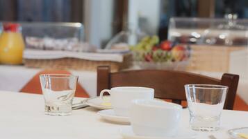 A breakfast table with clear glasses, a white cup, and a fruit bowl in the background.