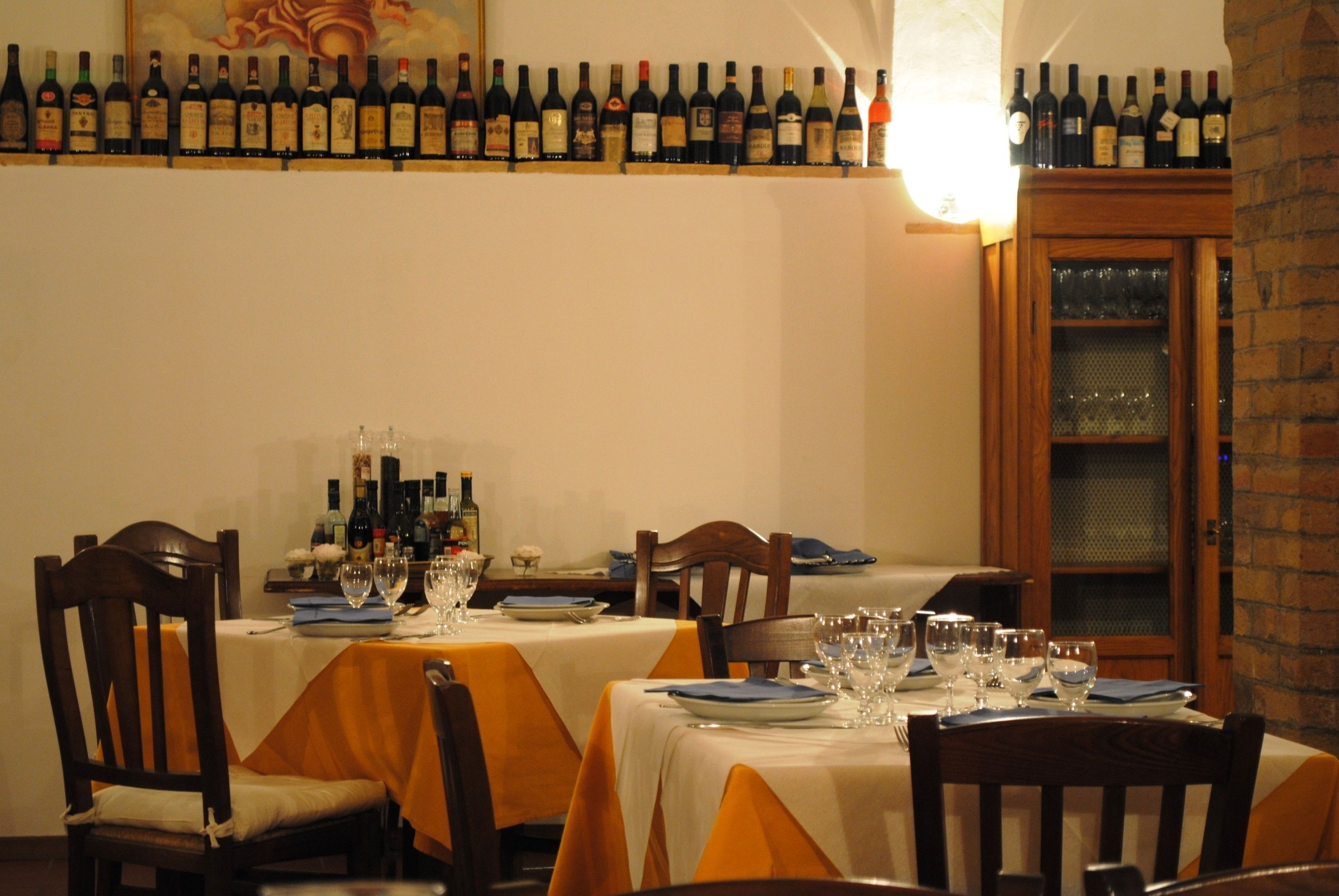 A restaurant with tables set for dining, wine bottles on the wall, and a brick wall.