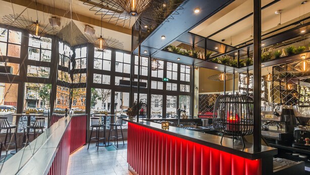 A modern bar area with a red accent wall, large windows, and a view of the cityscape. - Hotel Iron Horse (Amsterdam)