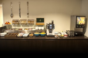 Tarjolla on monipuolinen buffet, jossa on erilaisia ruokia, kahviautomaatti ja digitaalinen ruokalista.
