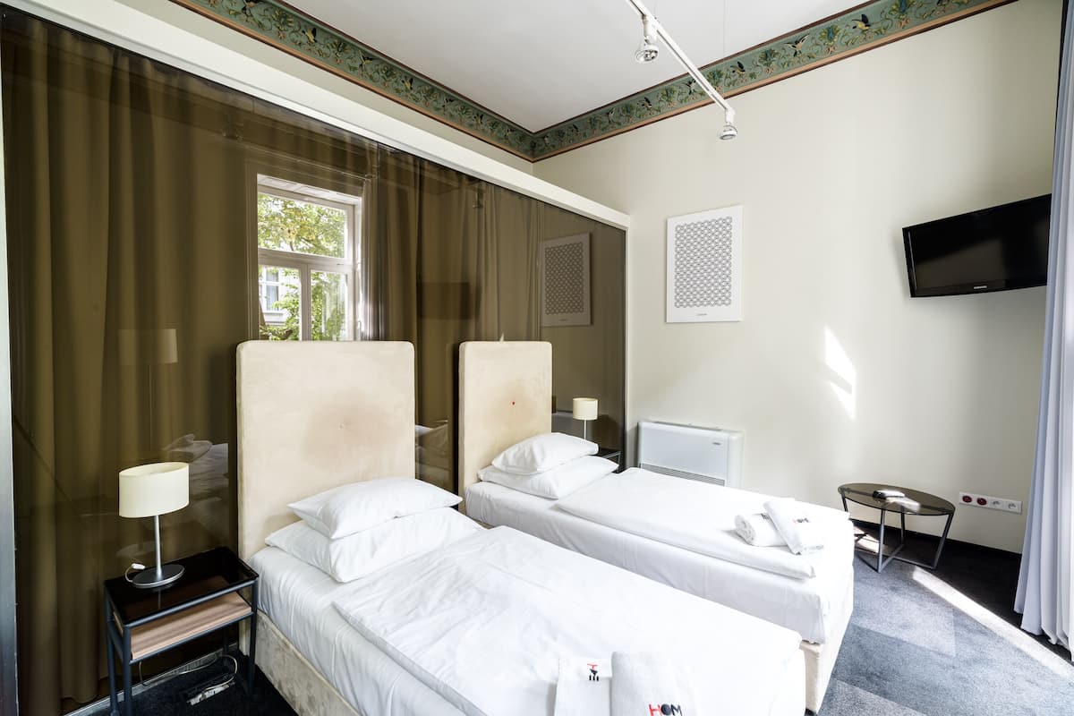A hotel room with two beds, a TV, a desk, and a window with curtains.