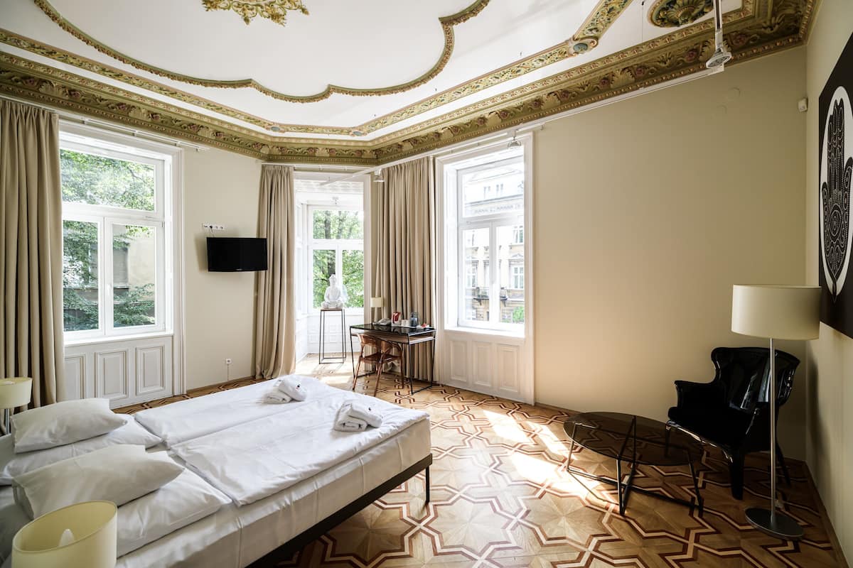 A hotel room with a large bed, a desk, a chair, a TV, and a lamp.