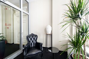 A room with a black leather chair, a white bust sculpture, a potted plant, and a small table. - Home ApartHotel (Kraków)