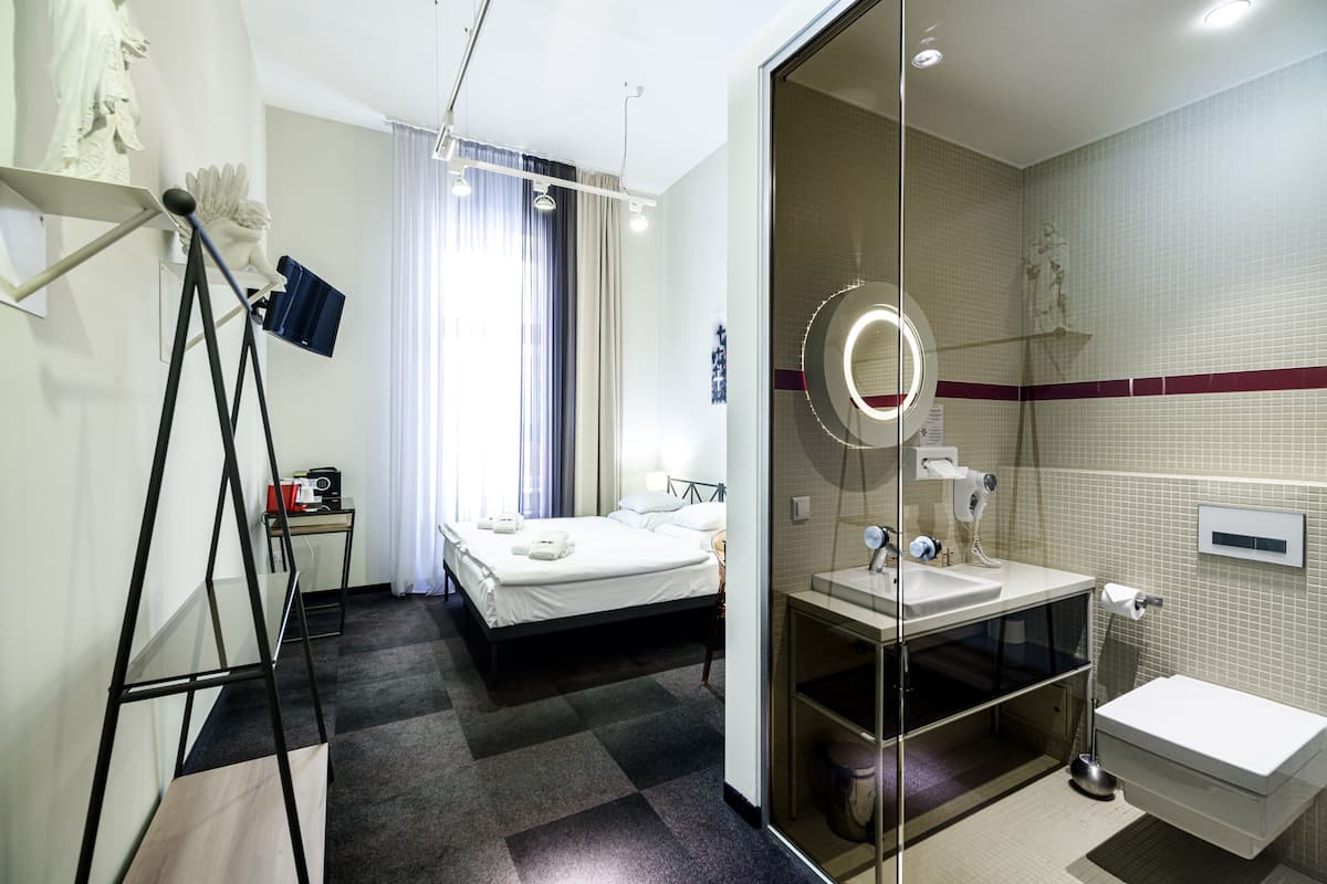 A hotel room with a bed, a bathroom with a mirror, and a small desk with a lamp.