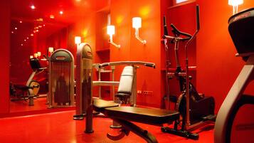 A gym with exercise equipment, mirrors, and red walls.