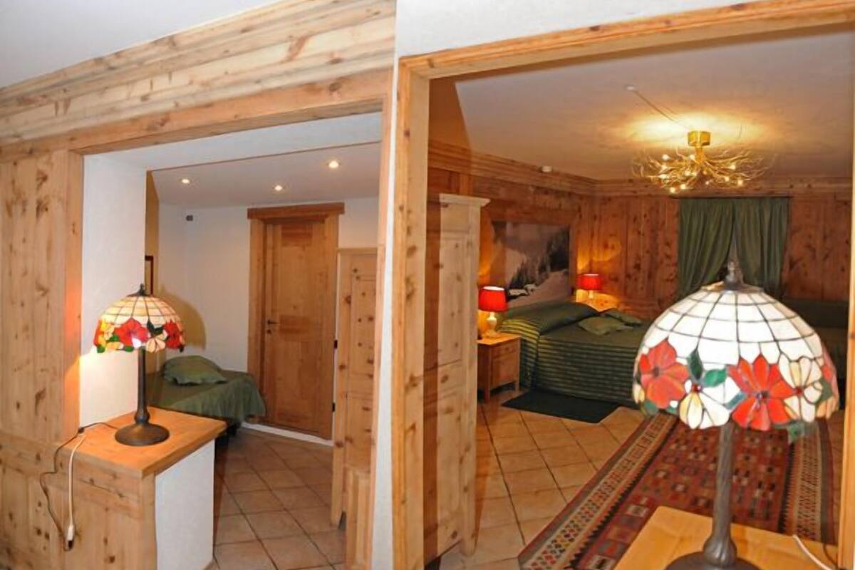Una stanza in legno con un letto, un comodino, una lampada e una porta che dà su un'altra stanza.