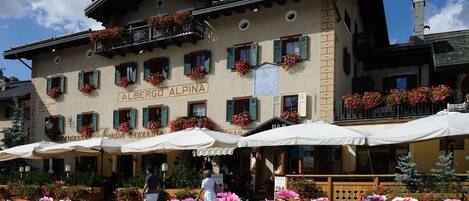 Un edificio con un letrero que dice "Alberg Alpina" y terraza exterior con sombrillas.