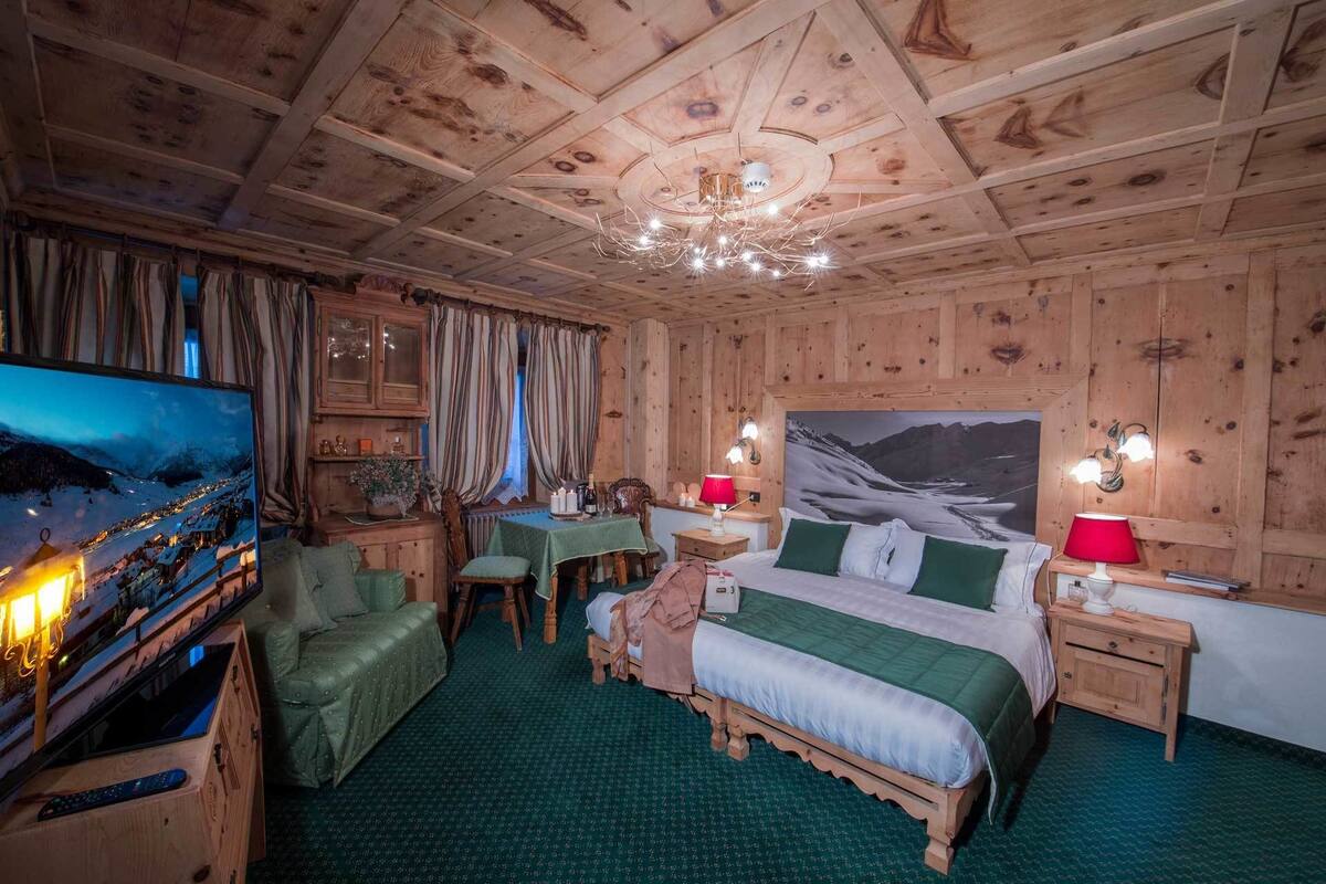 Accogliente camera da letto in legno con un letto, una scrivania, una sedia, una televisione e un lampadario.