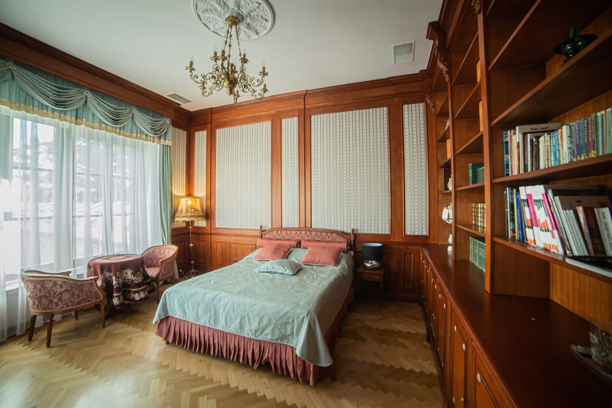 Ein klassisch eingerichtetes Zimmer mit einem großen Bett, einer Holzbücherreol und einem Schreibtisch mit Lampe.