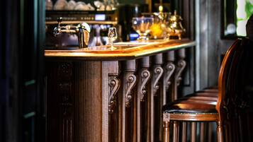 Zona de bar con mostrador de madera, taburetes y una lámpara colgante.