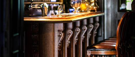 Zona de bar con mostrador de madera, taburetes y una lámpara colgante.