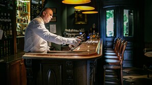 A bar with a bartender pouring a drink, wooden bar counter, and shelves of bottles. - Zamek Dubiecko (Dubiecko)