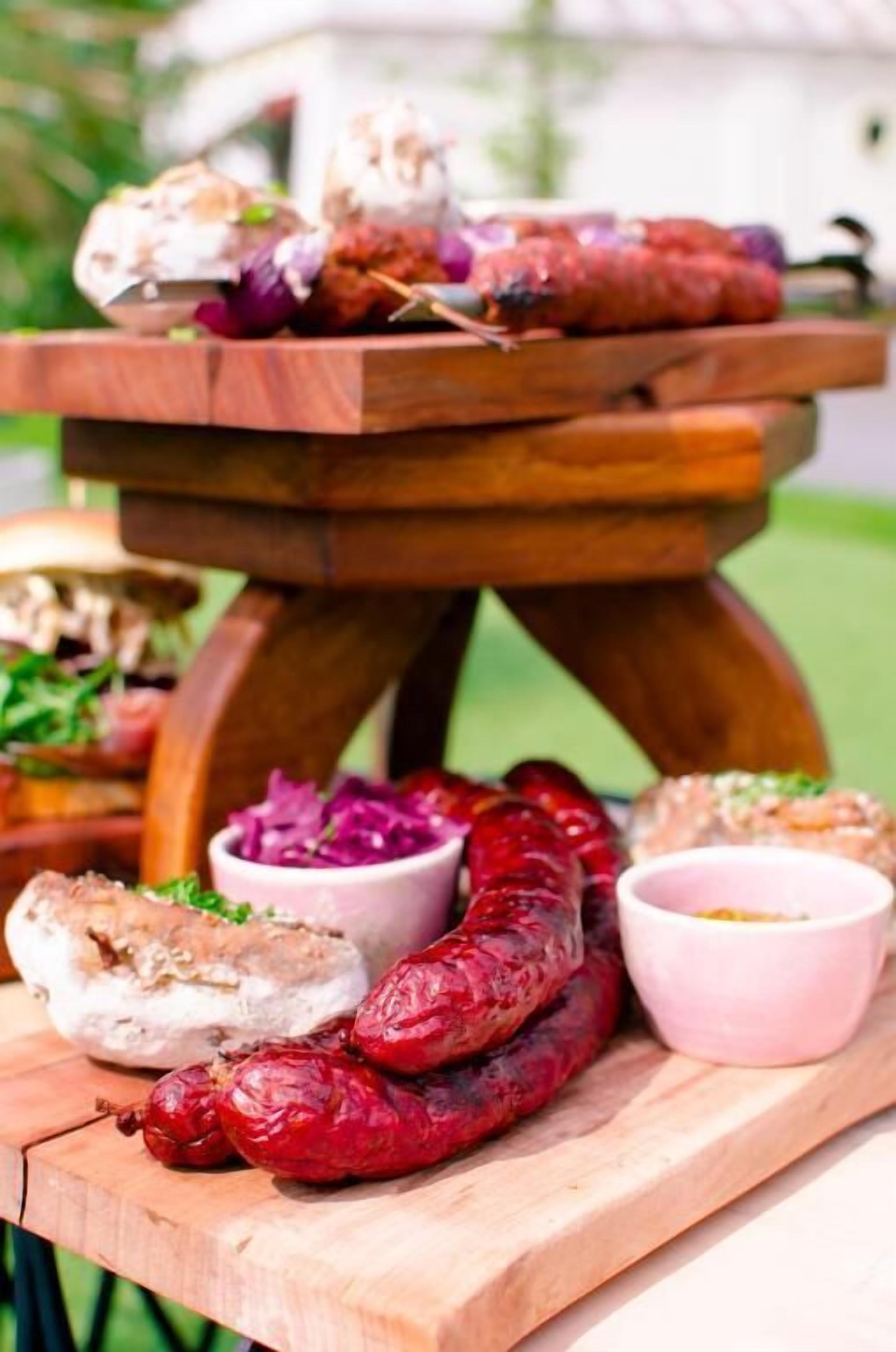 A wooden serving board with various food items, including sausages and a bowl of red cabbage.