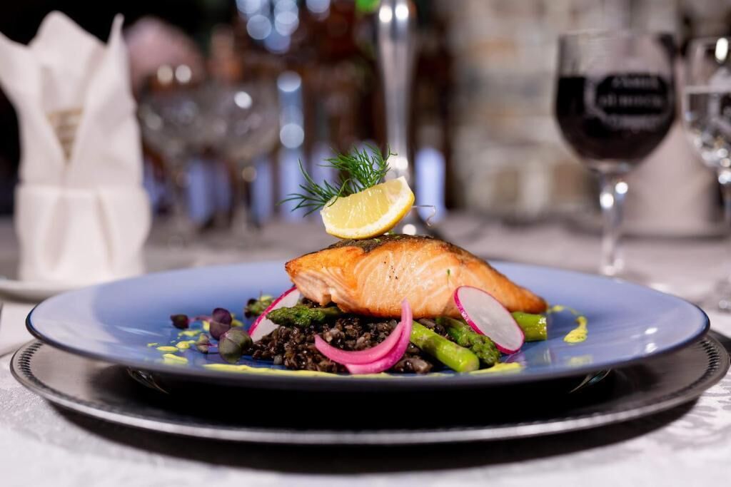 A plate of food with salmon, asparagus, and radishes, accompanied by a glass of red wine.