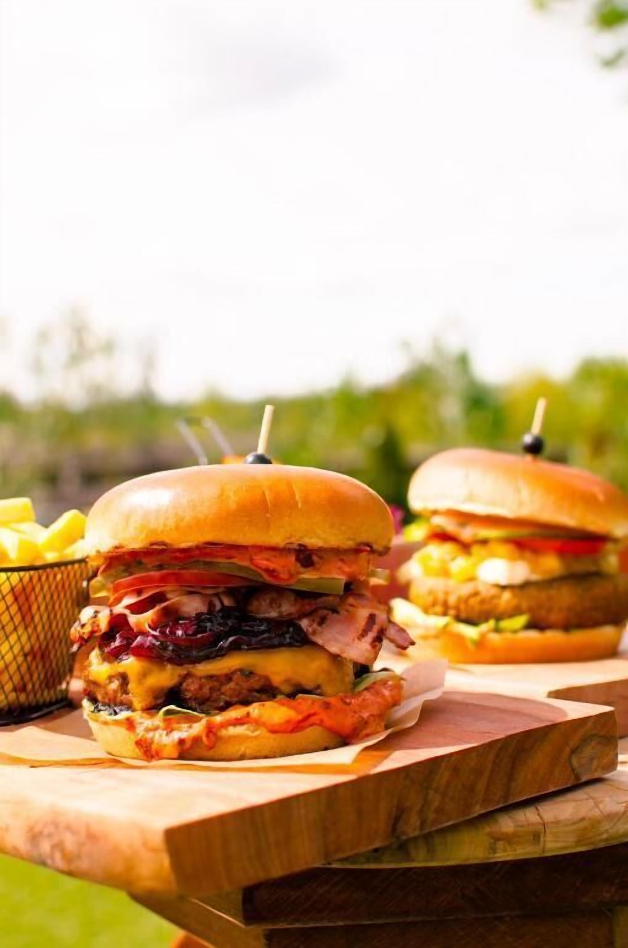 Two burgers on a wooden board with fries in a basket.