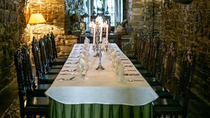 A long dining table set with candles and glasses, surrounded by chairs in a stone-walled room with a high arched ceiling. - Zamek Dubiecko (Dubiecko)
