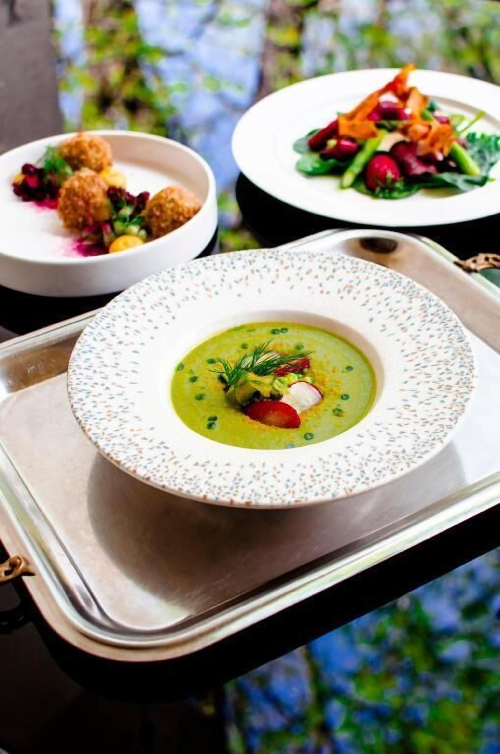 Una mesa de comedor con tres platos: un tazón de sopa adornado con hierbas, una ensalada con verduras y un plato de bolitas empanizadas acompañadas de salsa.
