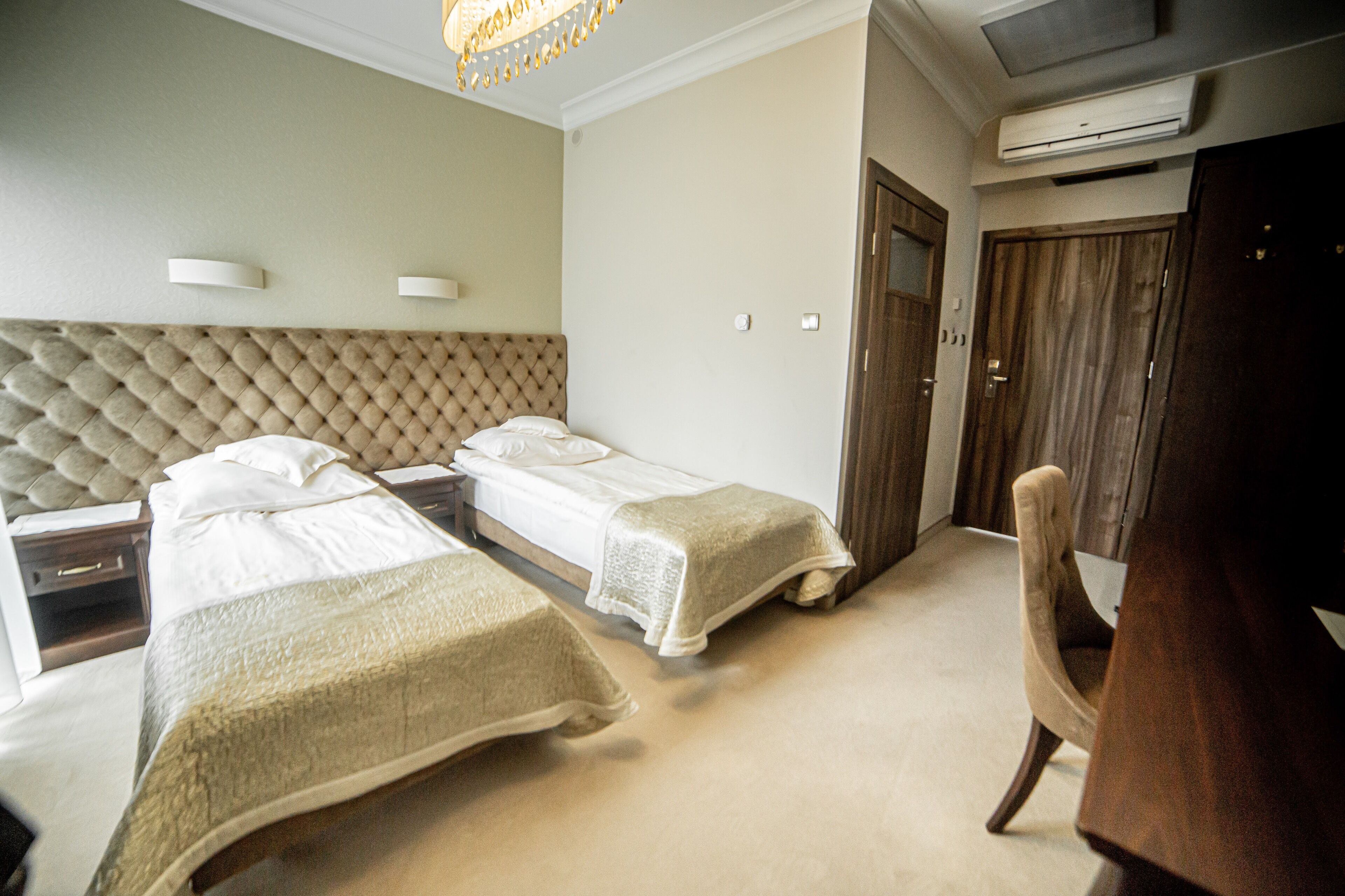 A hotel room with two beds, a wooden wardrobe, a chair, and a ceiling light fixture.