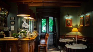 A bar area with wooden bar counter, bar stools, and hanging lamps. There is a window with a view of greenery outside. - Zamek Dubiecko (Dubiecko)