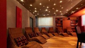 A room with wicker lounge chairs, a bookshelf, and a large window. - Hotel Isolabella Wellness (Primiero San Martino di Castrozza)