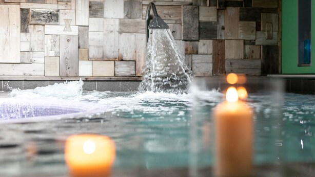 A hot tub with water jets, candles, and a wooden wall backdrop. - Hotel Isolabella Wellness (Primiero San Martino di Castrozza)