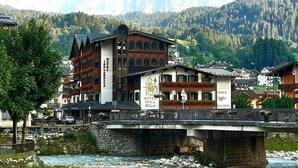 A hotel with a stone bridge over a river, surrounded by mountains and greenery. - Hotel Isolabella Wellness (Primiero San Martino di Castrozza)