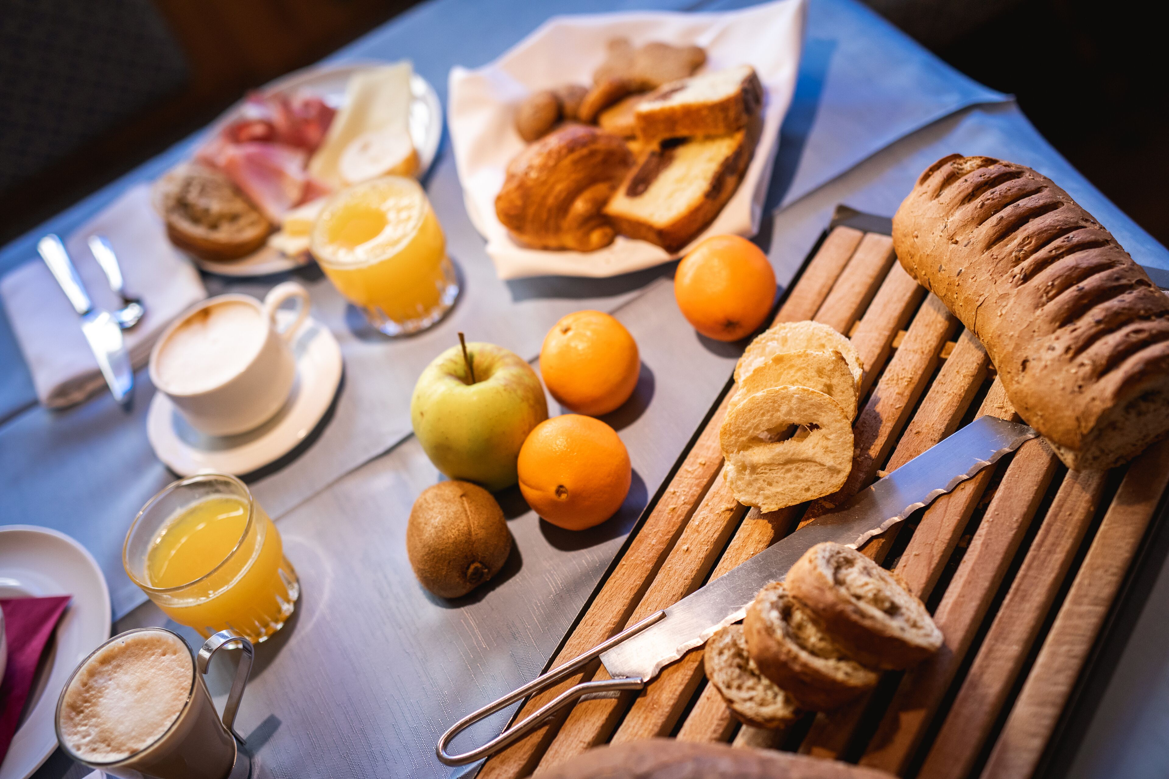 Un plateau de petit-déjeuner avec des croissants, du pain, des pommes, des oranges et un couteau.