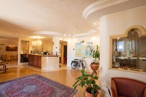 A spacious hotel lobby with a reception desk, a dining area, and a large rug.