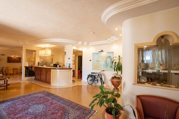 A spacious hotel lobby with a reception desk, a dining area, and a large rug.