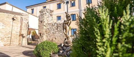 Un patio con una estatua de piedra, un edificio con múltiples ventanas y un camino pavimentado.