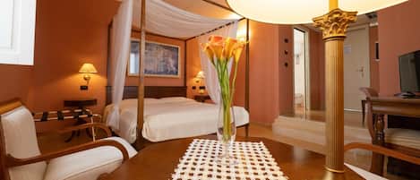 Una habitación de hotel con una cama con dosel, una zona de estar con una mesa y sillas, y una lámpara de pie grande.