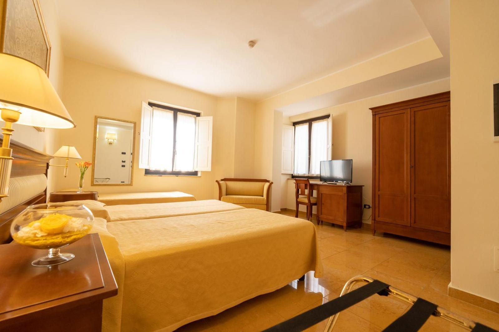 Una camera d'albergo con due letti, una scrivania con televisore e un armadio.